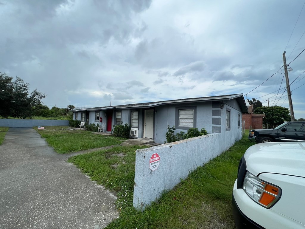 A white car is parked in front of a grey house with a red sticker on the wall.