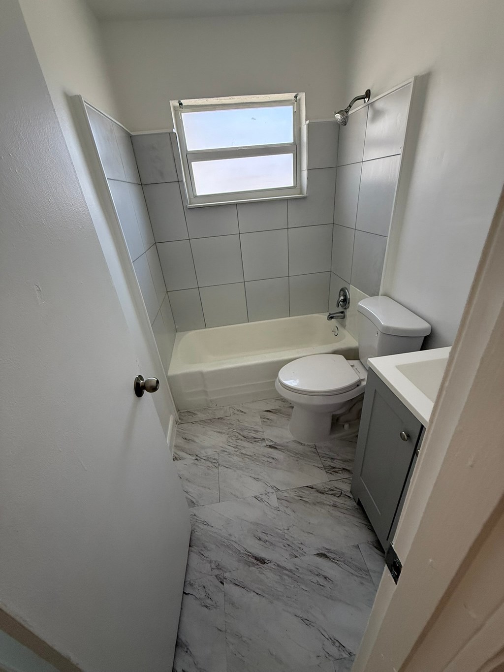 A white toilet sits in a bathroom with a marble floor and a window above it.