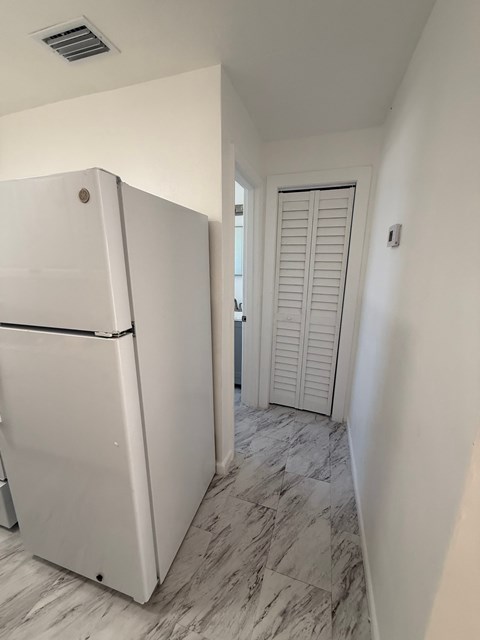 A white refrigerator in a kitchen with a marble floor.