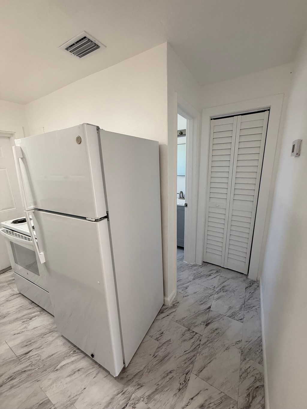 A white refrigerator in a kitchen with a marble floor.