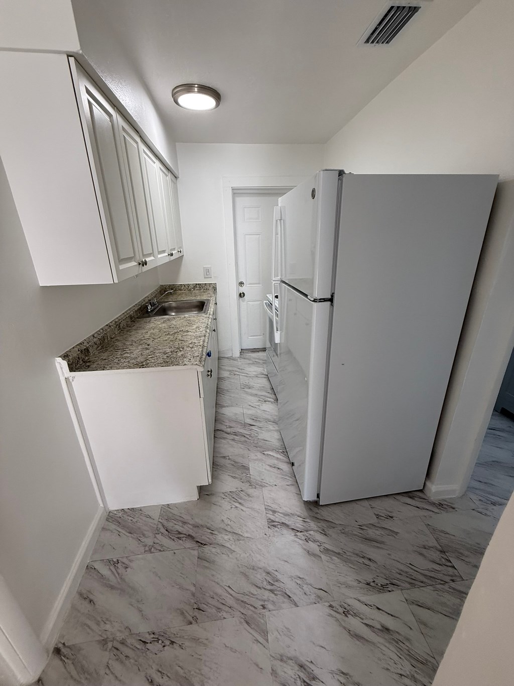 A kitchen with white cabinets and a marble floor.