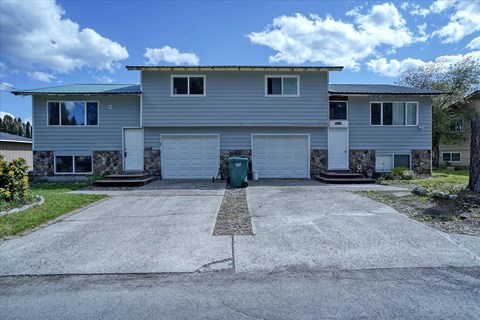 A grey house with a white garage door and a green trash bin in front.