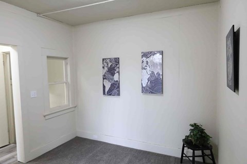 A room with two paintings on the wall and a plant on a stool.