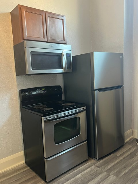 A kitchen with a black stove and oven, a microwave above it, and a silver refrigerator to the right.