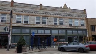 A grey car is parked in front of a building with a blue sign.