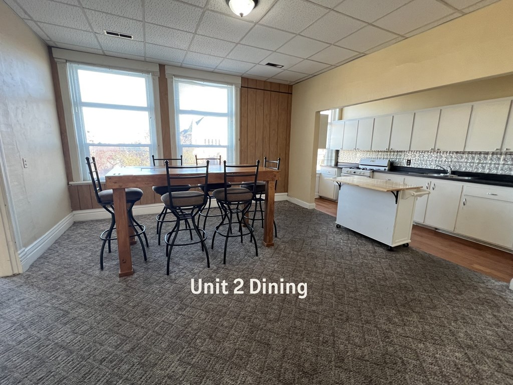 A dining area with a table and chairs in a room with a kitchen in the background.