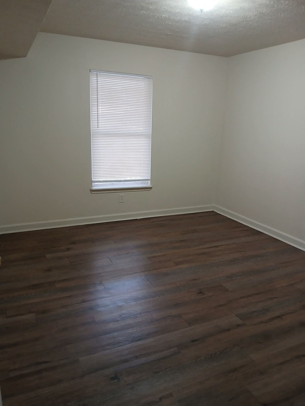 A room with wooden flooring and a window with blinds.