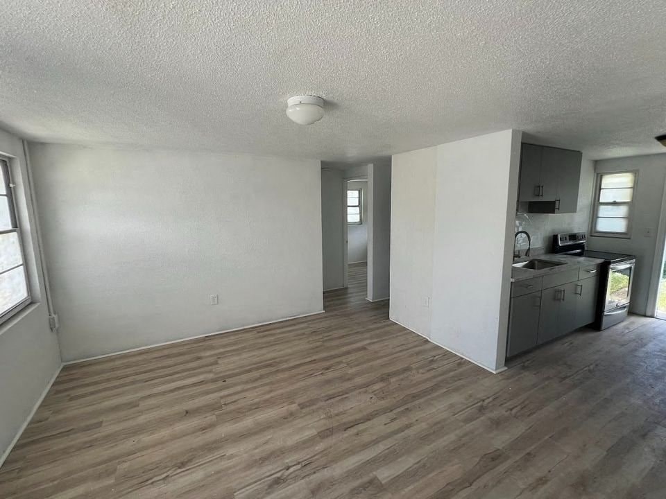 A room with wooden flooring and a kitchen area in the background.
