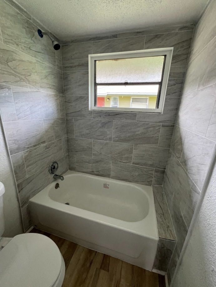 A white toilet sits next to a bathtub in a bathroom with grey tiles.