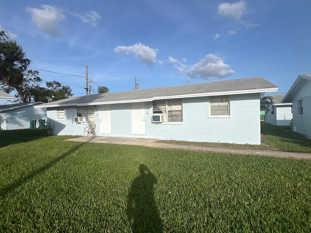 A house with a blue exterior and a grey roof is surrounded by a green lawn.