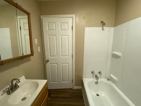 A white bathroom with a sink, mirror, and bathtub.