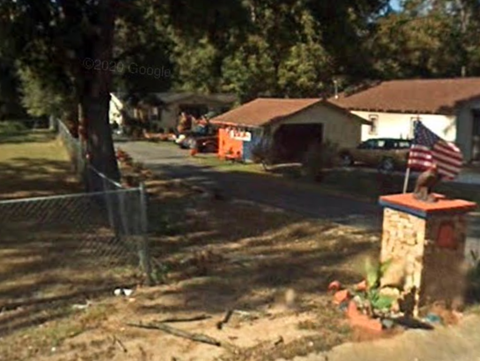 A residential street with a house and a flag on the right.