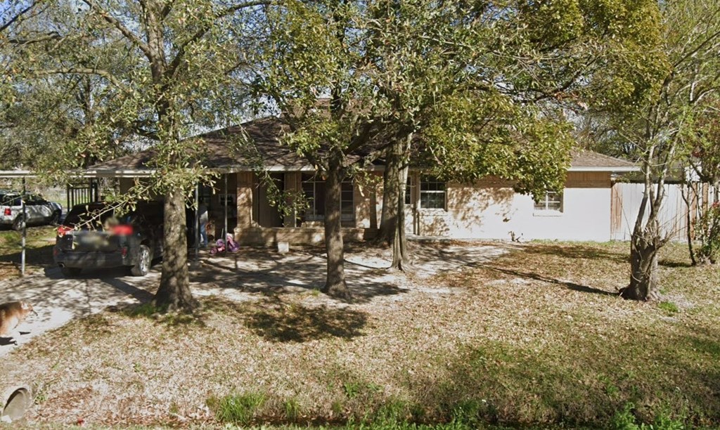 A house with a brown roof and a white wall is surrounded by trees and grass.