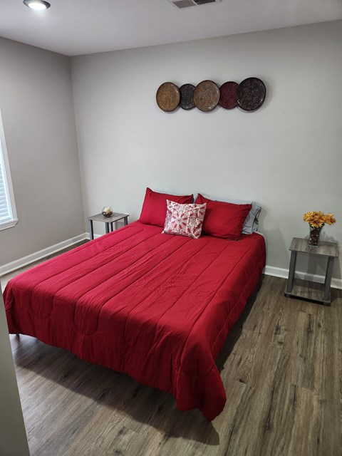 a bedroom with a red bed and white walls and wood floors