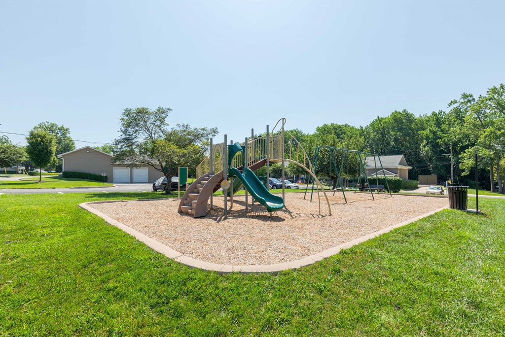 A playground with a green slide and brown sandbox.