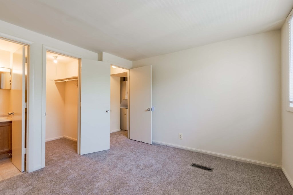 A room with carpeted floor and white walls with a doorway leading to another room.