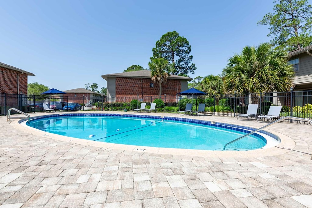 A swimming pool surrounded by a brick patio and a black fence.