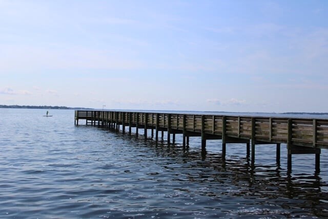 A wooden pier extends into a calm body of water under a clear blue sky.