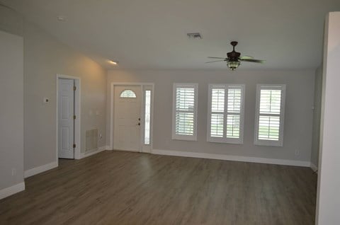 an empty living room with a ceiling fan and windows