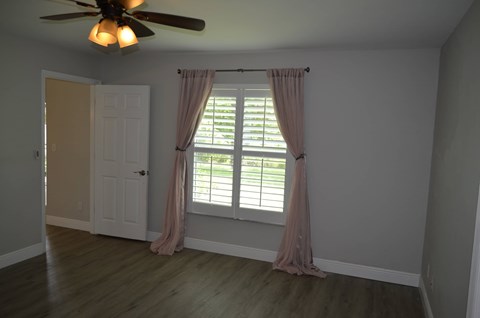 a window with pink curtains in a room with a door and a ceiling fan