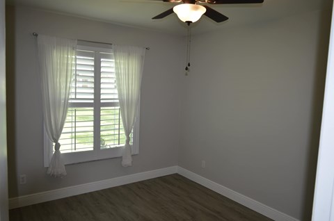 a bedroom with a ceiling fan and window with white curtains