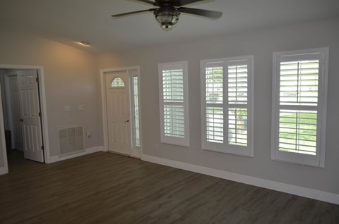 an empty living room with a ceiling fan and windows