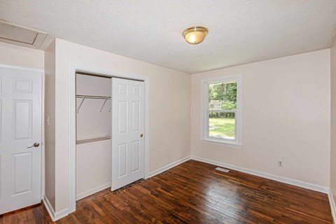 A room with a white door and a window with a view of a lawn and trees.