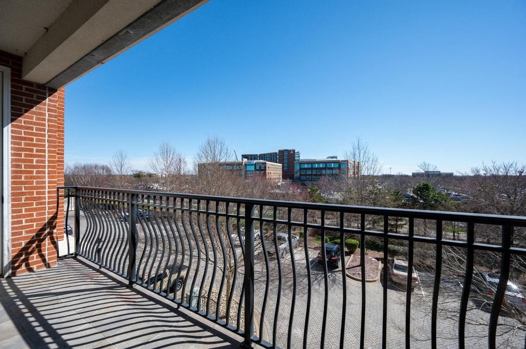 A balcony with a black railing overlooks a parking lot and buildings.