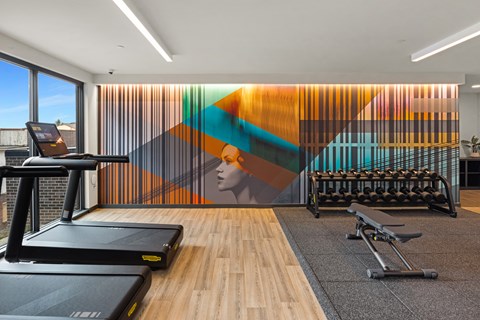A gym with treadmills, weights and a colorful mural on the wall.