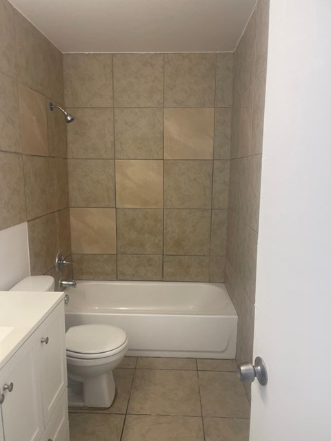 A white toilet sits next to a white bathtub in a tiled bathroom.