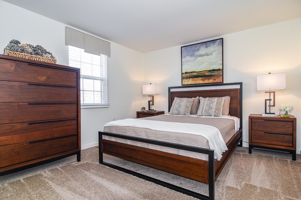 A bedroom with a large bed, a dresser, and a nightstand with lamps.