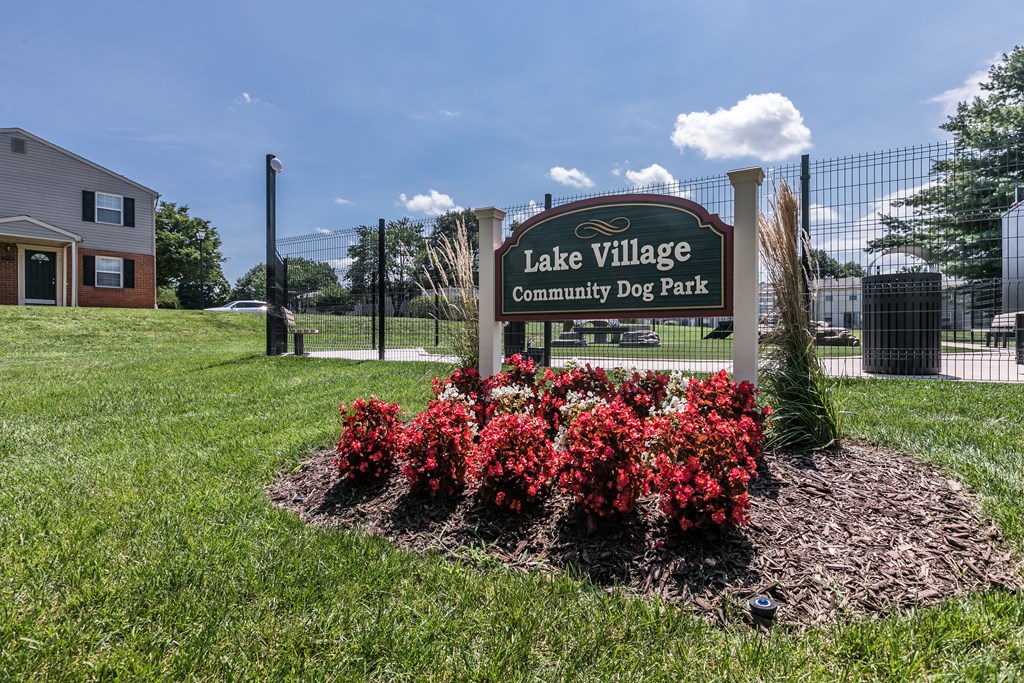 A sign for Lake Village Community Dog Park stands in a flower bed.
