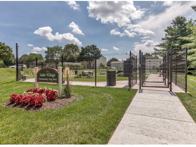 The image shows the entrance to Lake Village Community Dog Park with a sign and a metal gate.