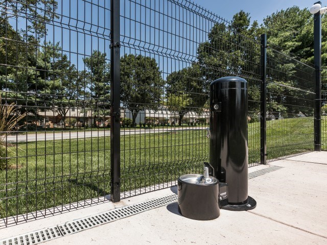A black fence with a metal trash can and a trash can lid on the ground.