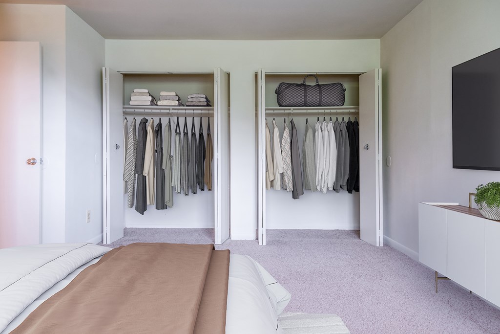 A bedroom with a bed and a closet with clothes hanging.