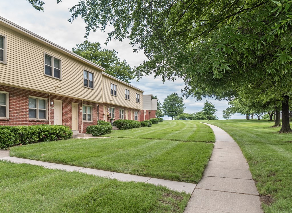 A row of houses with green lawns and trees in front.