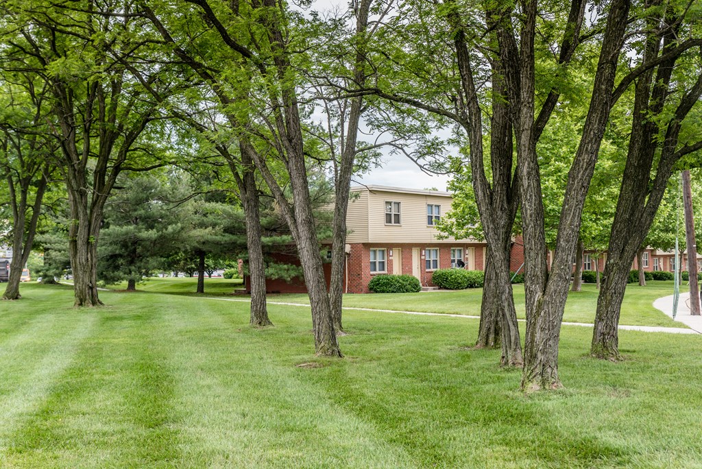 A house is surrounded by trees in a grassy area.