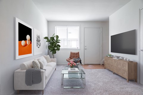 A modern living room with a grey sofa, a glass coffee table, a wooden cabinet, and a large painting on the wall.