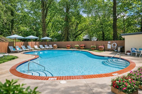 A pool surrounded by trees and chairs.