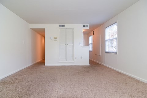 a spacious living room with white walls and carpet and a window