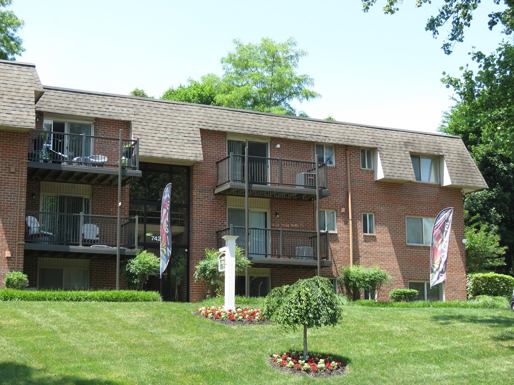 A red brick building with a balcony and a small garden in front.