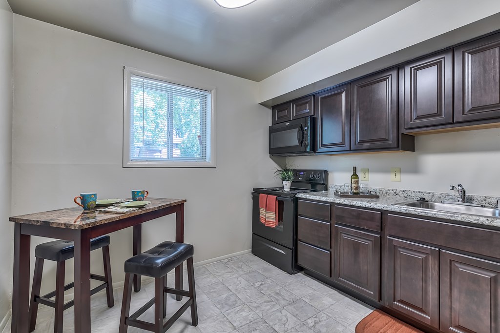 A kitchen with dark brown cabinets and a wooden table with two stools.