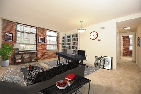 A living room with a black sofa and a coffee table with a bowl of fruit on it.