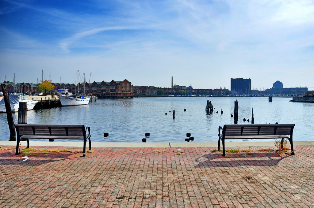 Two benches are on a brick walkway by a body of water.