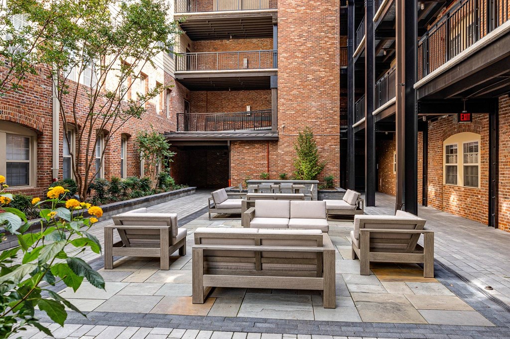 A patio with wooden furniture and a brick building in the background.
