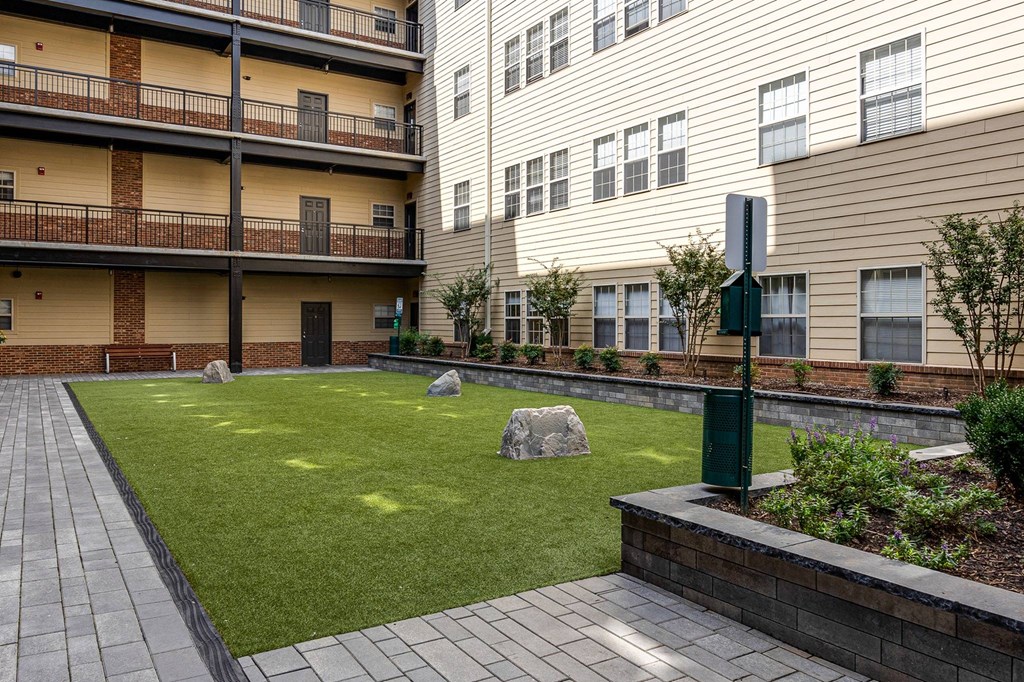 A grassy area in front of apartment buildings with a small garden and a trash can.