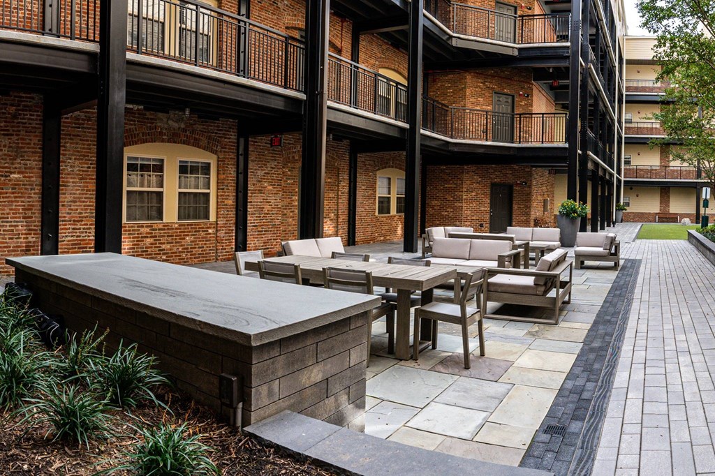 A patio with tables and chairs is surrounded by brick buildings.