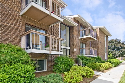 A brick apartment building with balconies and bushes in front.