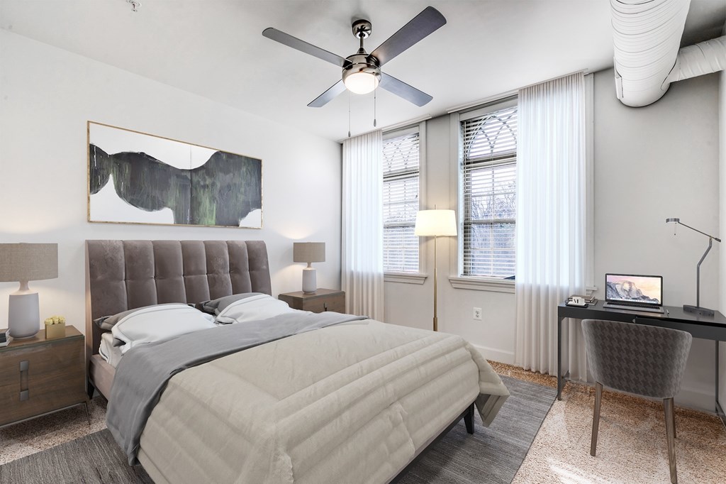 A bedroom with a large bed, a desk, and a ceiling fan.