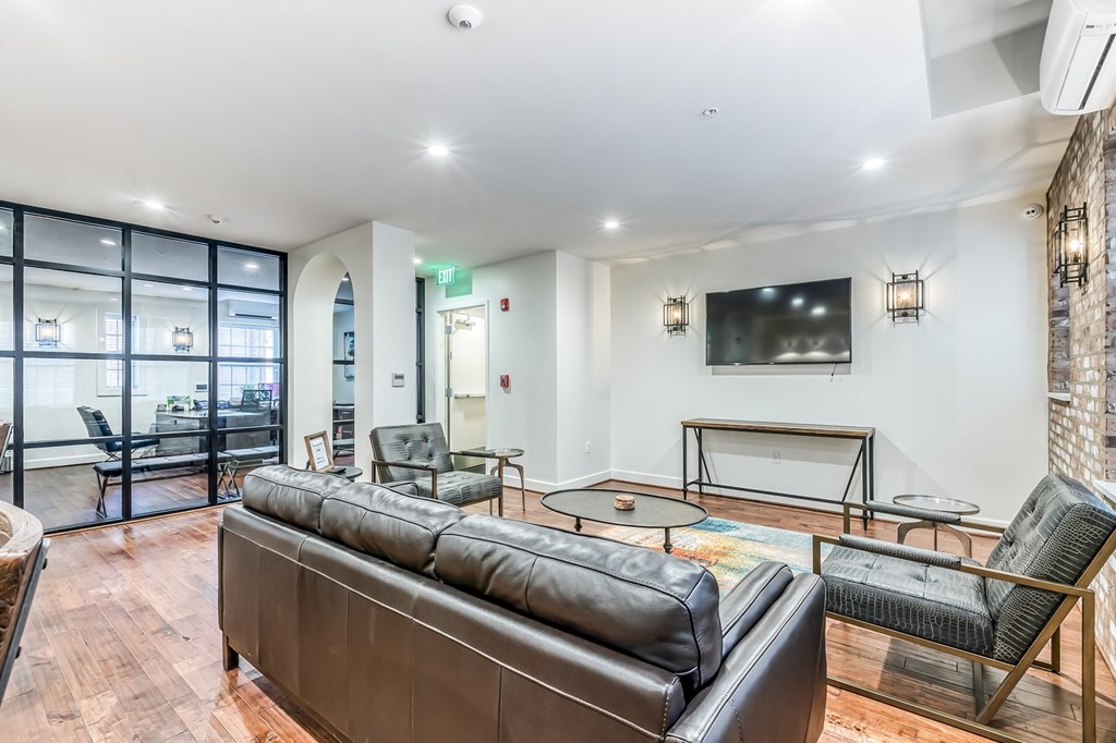 A living room with a black leather couch and a flat screen TV mounted on the wall.